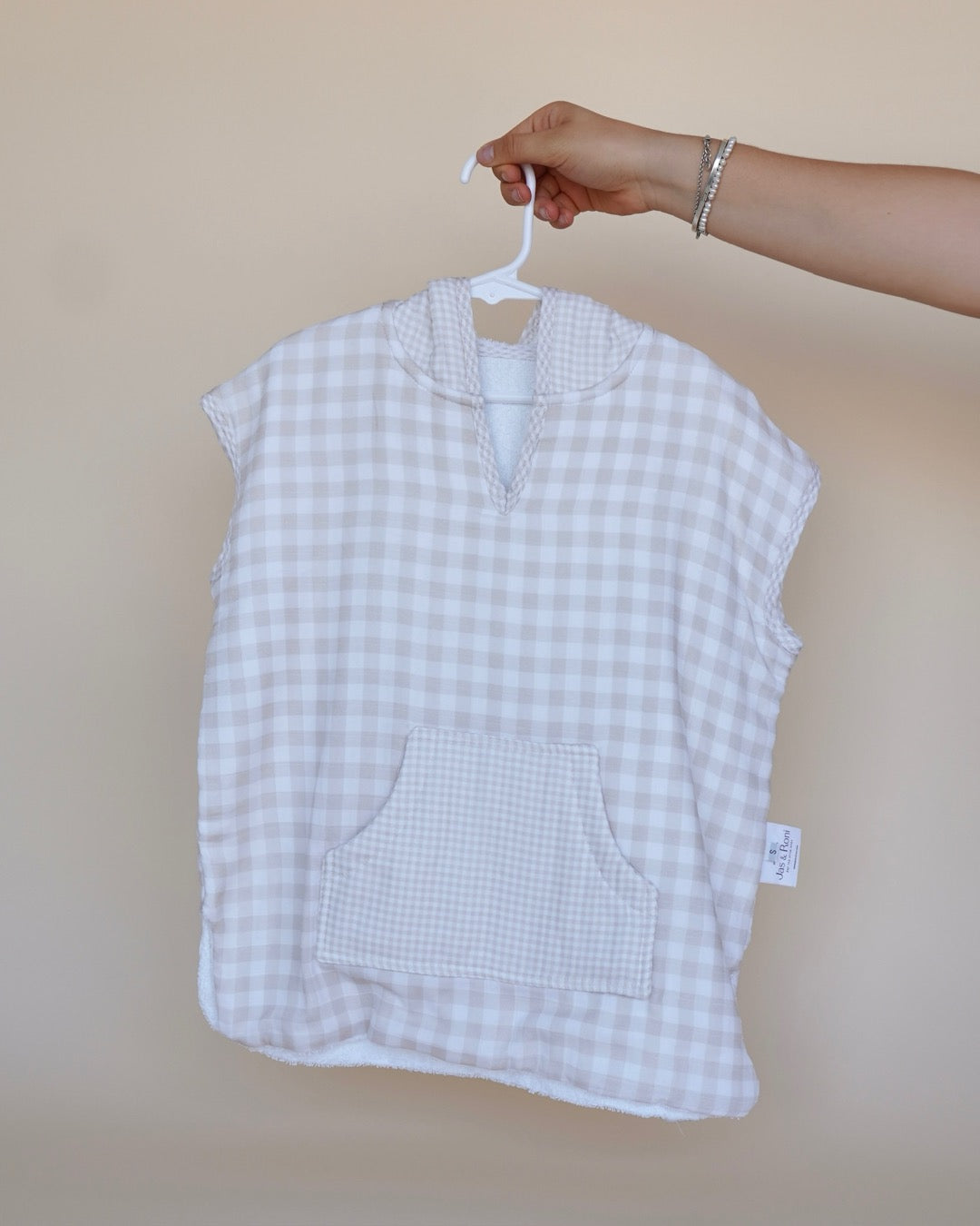Poncho de toalla y muselina en gancho sostenido por una mano en beige squares