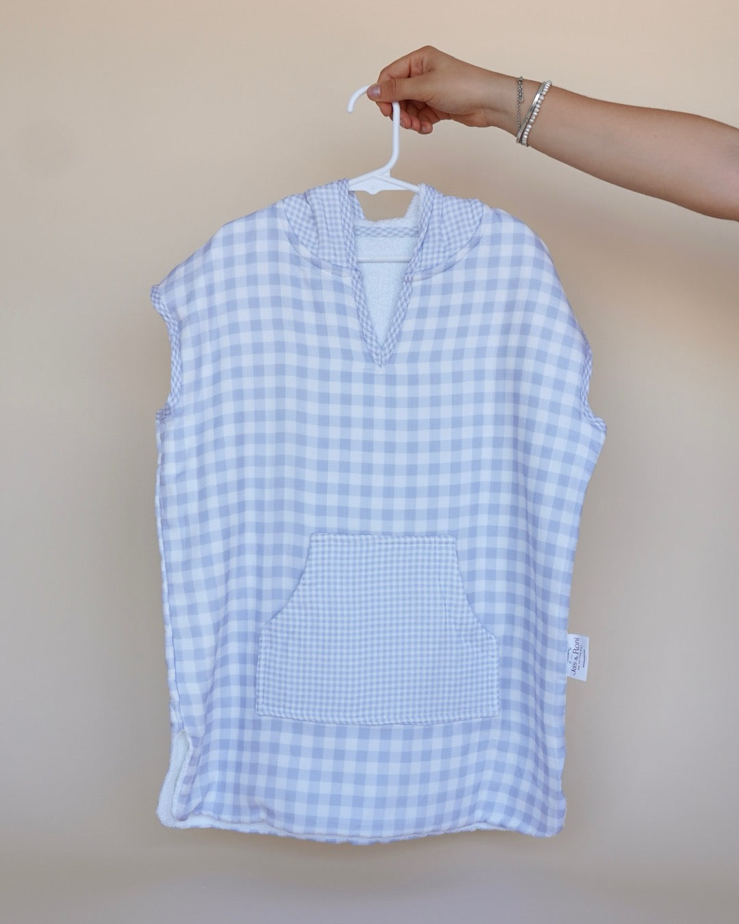 Poncho de toalla y muselina en gancho sostenido por una mano estampado en  cuadros azules