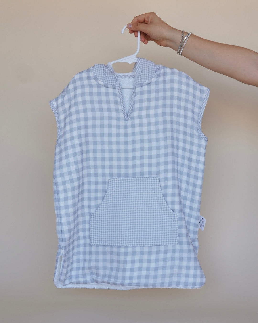 Poncho de toalla y muselina en gancho sostenido por una mano estampado en  cuadros grises