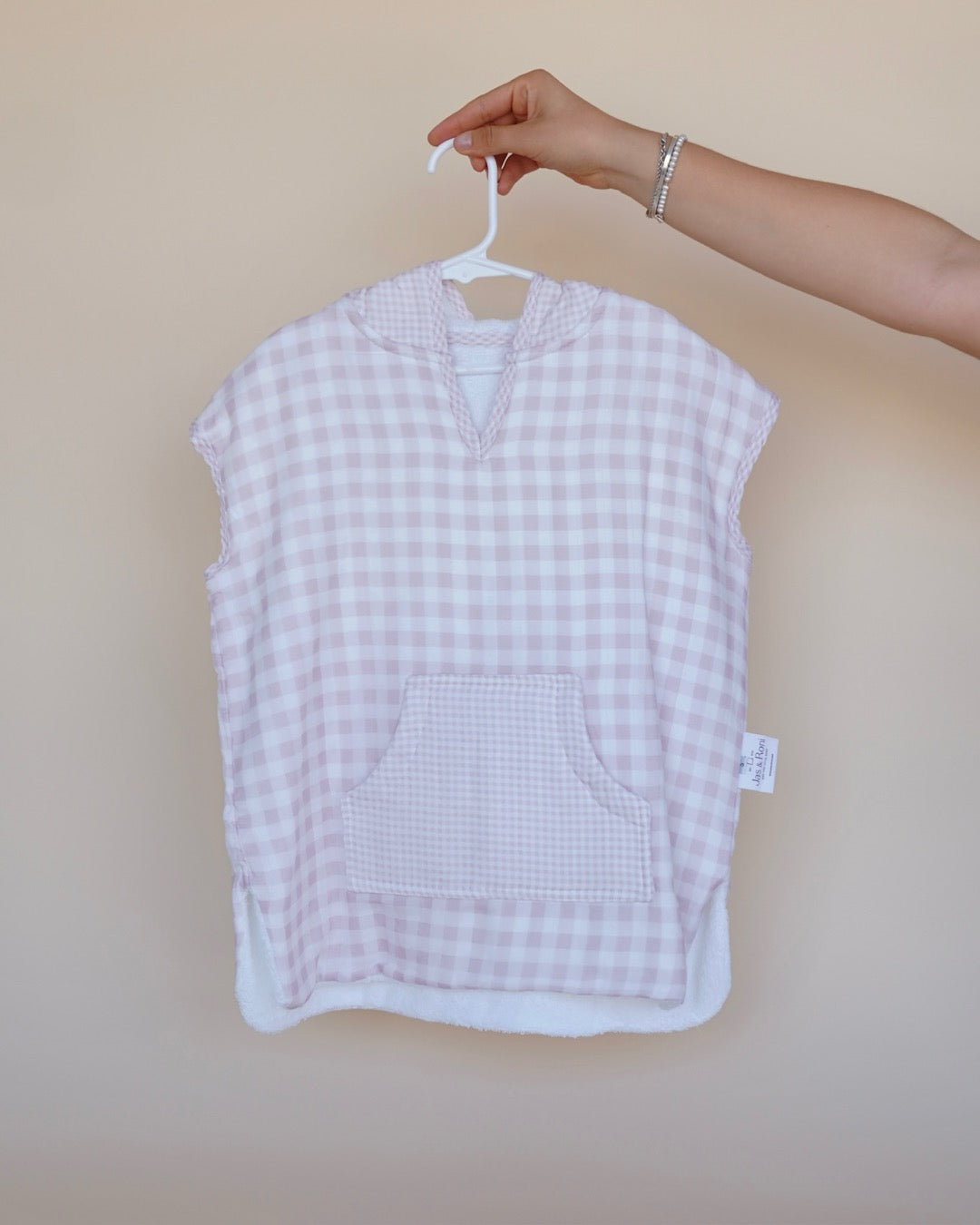 Poncho de toalla y muselina en gancho sostenido por una mano estampado en cuadros rosas