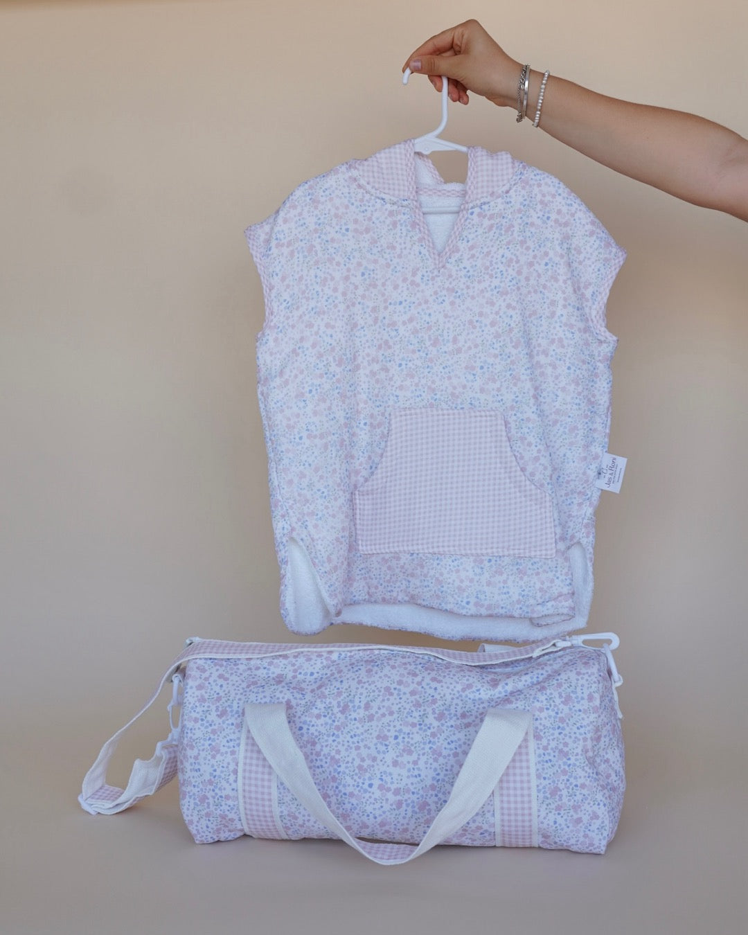 Poncho de toalla y muselina en gancho sostenido por una mano estampado en little flowers y pañalera de la misma tela