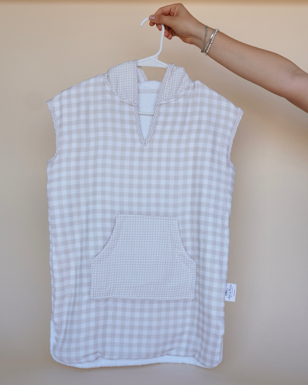 Poncho de toalla y muselina en gancho sostenido por una mano en beige squares large