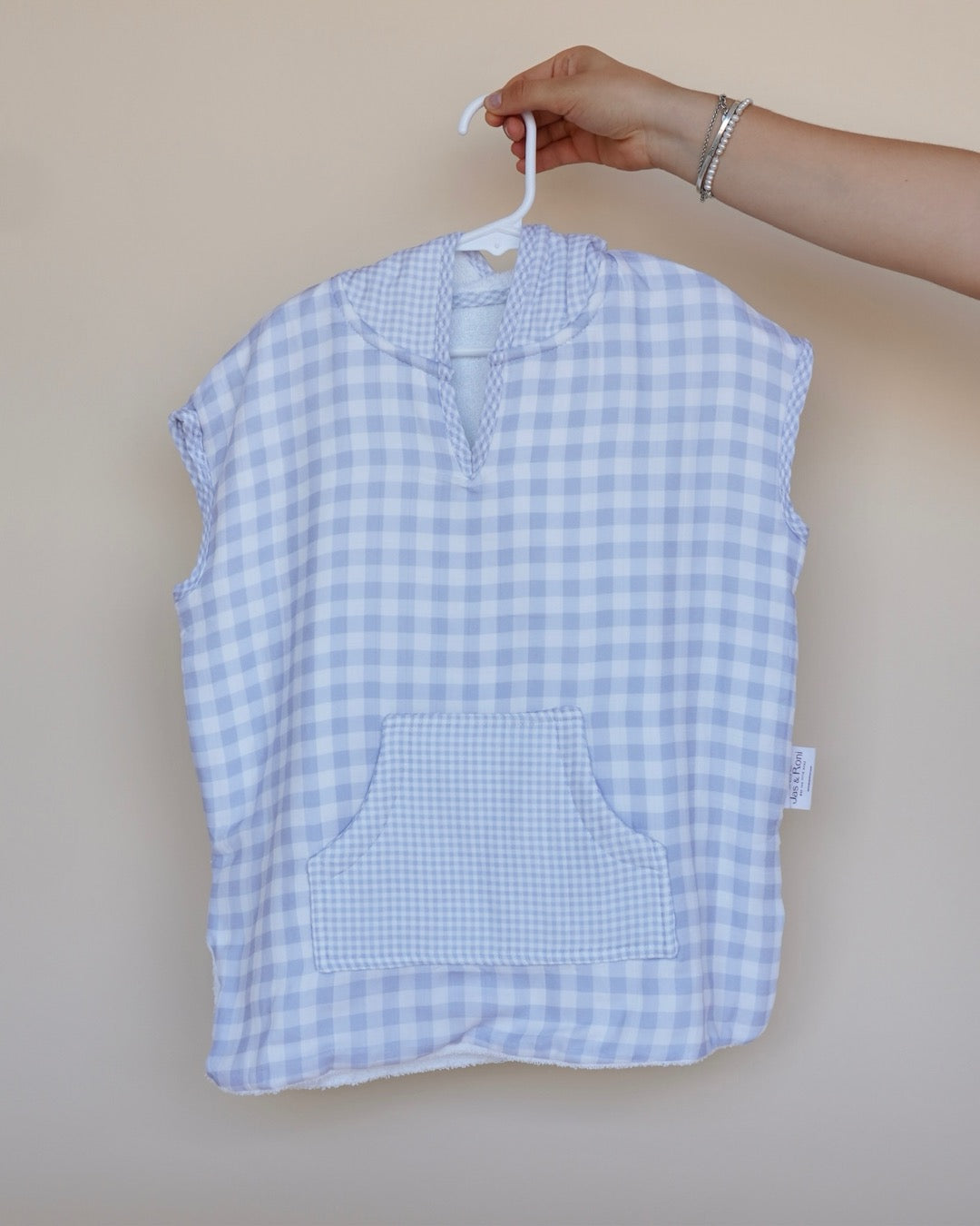 Poncho de toalla y muselina en gancho sostenido por una mano estampado en  cuadros azules 