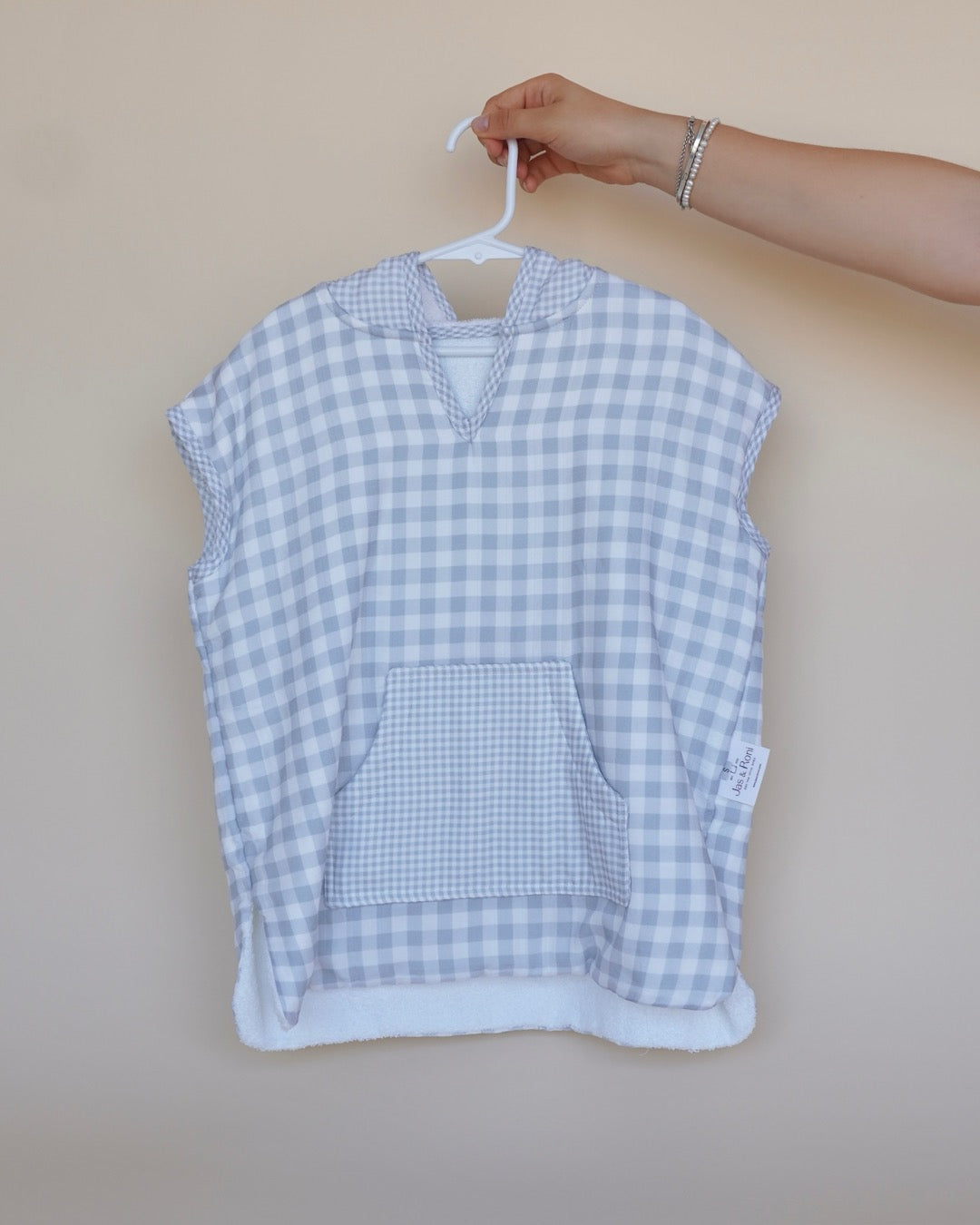 Poncho de toalla y muselina en gancho sostenido por una mano estampado en  cuadros grises