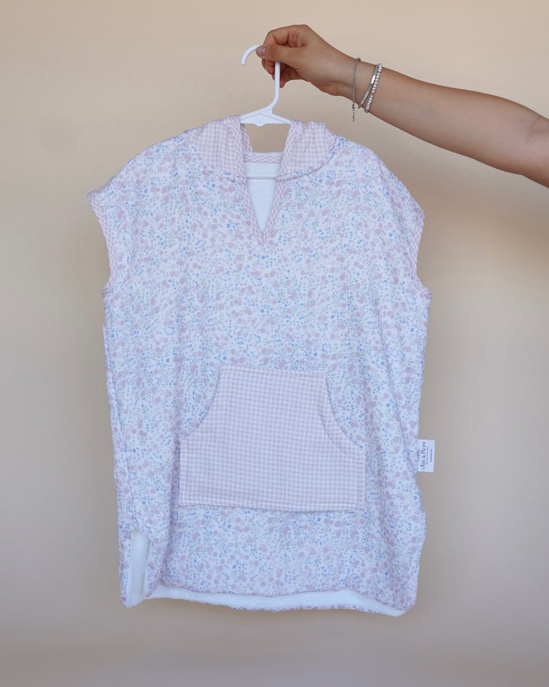 Poncho de toalla y muselina en gancho sostenido por una mano estampado en little flowers