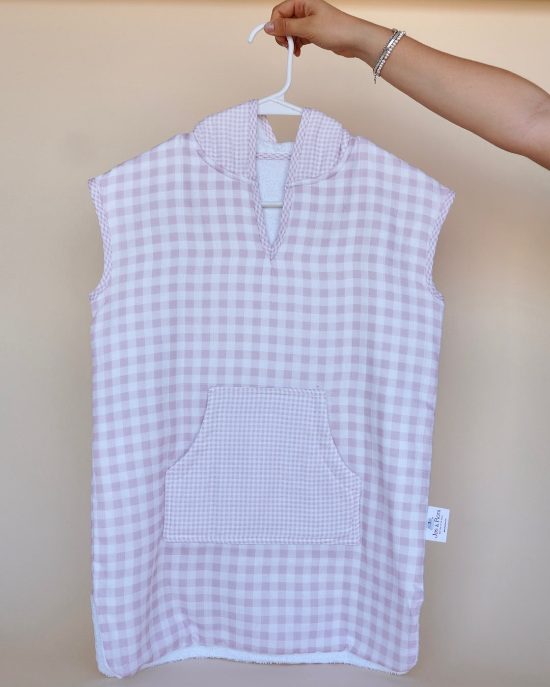 Poncho de toalla y muselina en gancho sostenido por una mano estampado en cuadros rosas