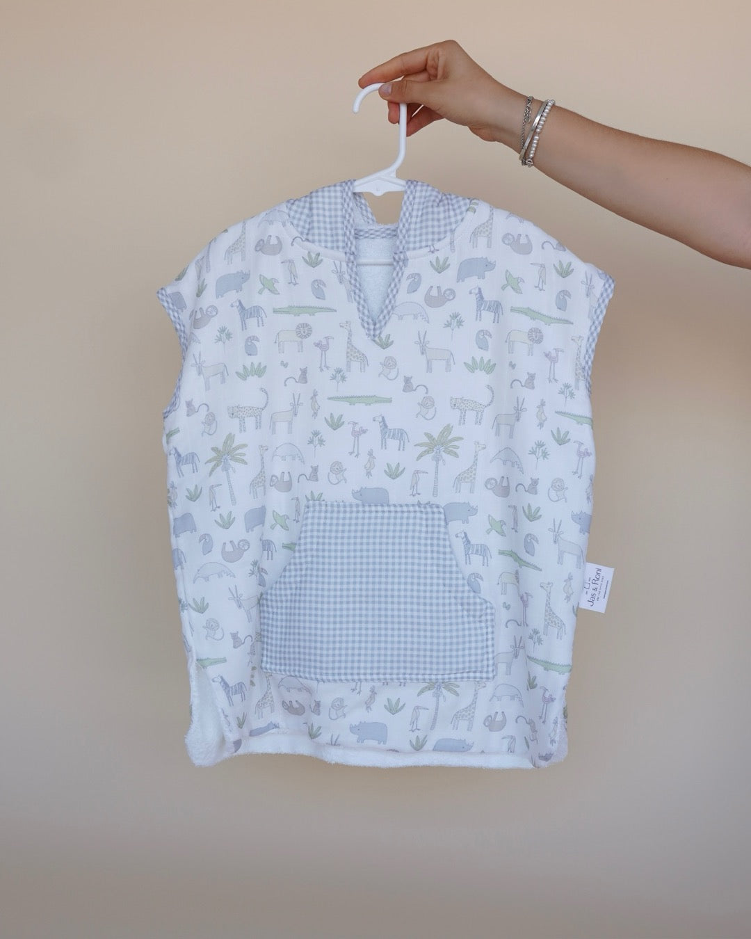 Poncho de toalla y muselina en gancho sostenido por una mano estampado en cuadros rosas