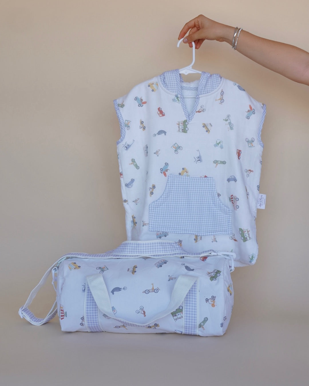 Poncho de toalla y muselina en gancho sostenido por una mano estampado en  carritos y pañalera en la misma tela